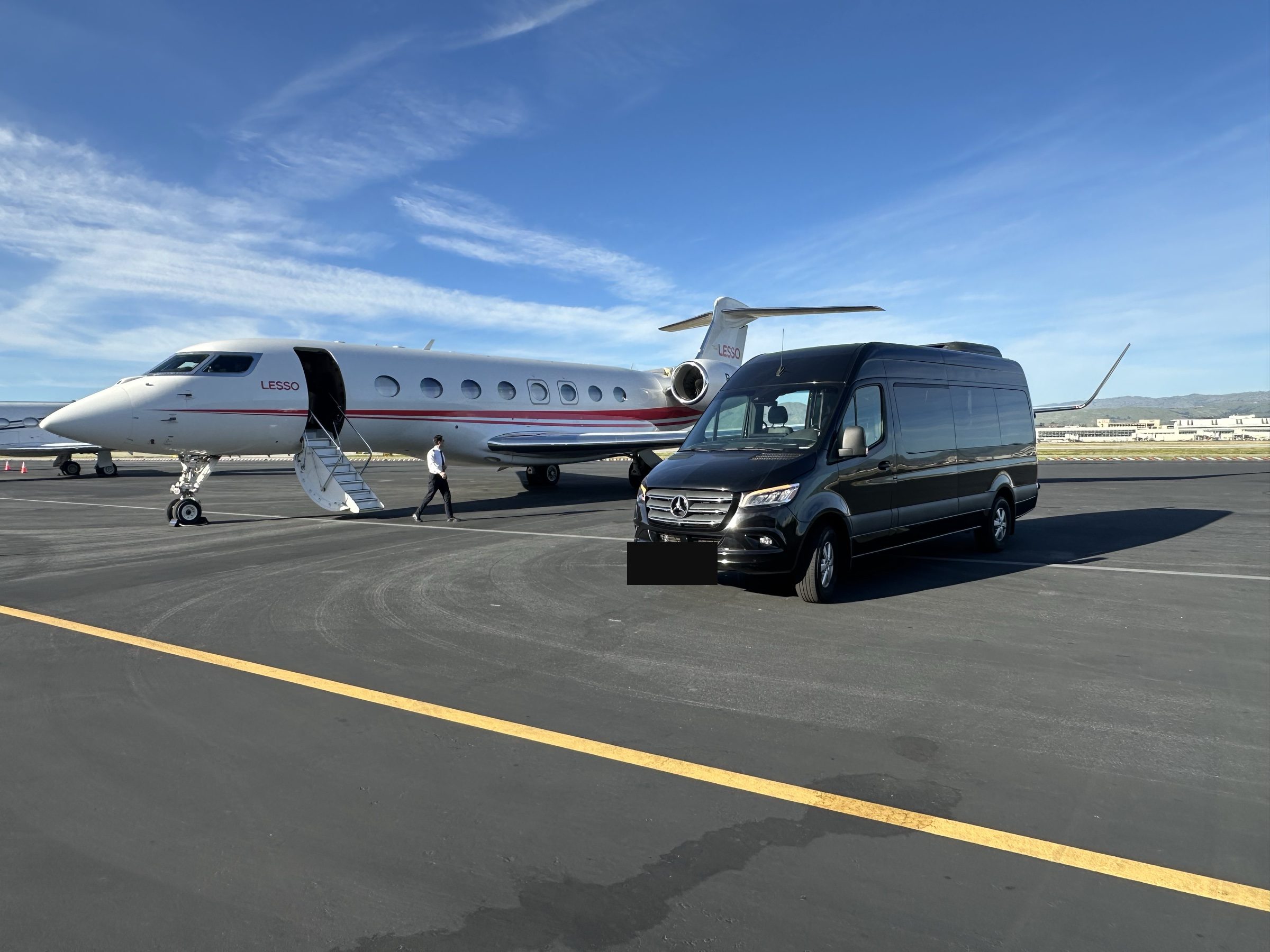 Black Mercedes Sprinter van beside a private jet